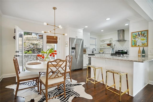 kitchen featuring wall chimney exhaust hood, stainless steel appliances, an inviting chandelier, pendant lighting, and white cabinets