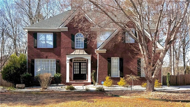 view of front of house with fence, brick siding, french doors, and a shingled roof