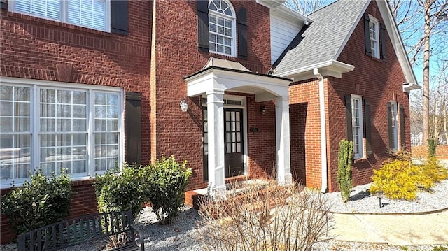 view of exterior entry with brick siding and roof with shingles