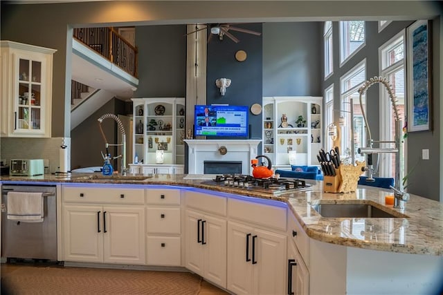 kitchen with light stone countertops, a towering ceiling, a ceiling fan, appliances with stainless steel finishes, and a sink