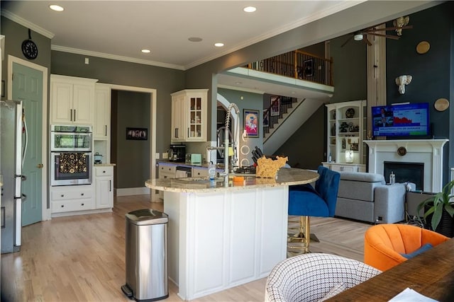 kitchen with light wood-style floors, ceiling fan, light stone countertops, a kitchen bar, and appliances with stainless steel finishes