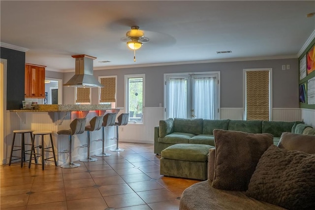 living area with ceiling fan, light tile patterned floors, ornamental molding, visible vents, and wainscoting