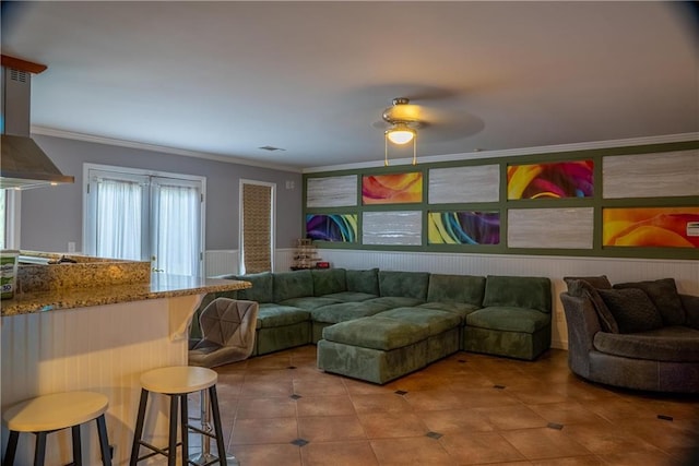 living room featuring crown molding, a ceiling fan, tile patterned flooring, and wainscoting