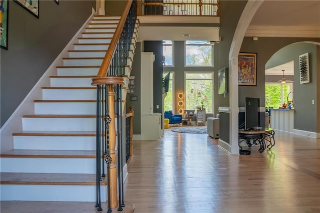 stairway featuring ornamental molding, baseboards, arched walkways, and wood finished floors