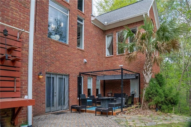 rear view of property featuring a patio area, brick siding, and roof with shingles