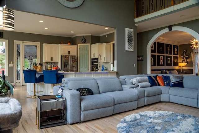 living area featuring recessed lighting, arched walkways, light wood-type flooring, and crown molding