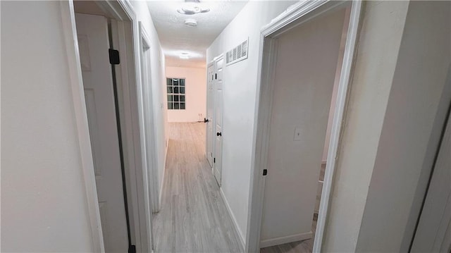 hallway with light hardwood / wood-style floors and a textured ceiling