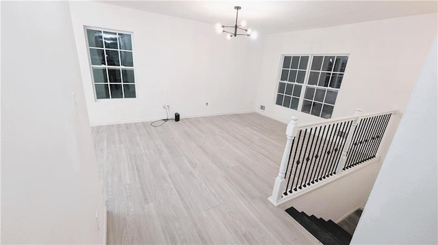 spare room featuring a notable chandelier and light wood-type flooring