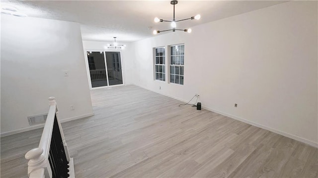 unfurnished room featuring light wood-type flooring and an inviting chandelier