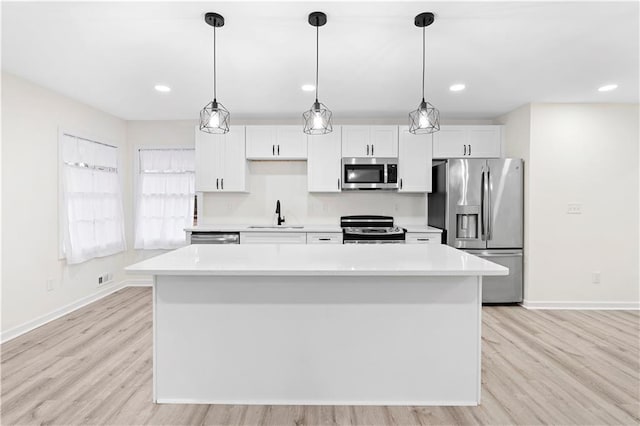 kitchen with appliances with stainless steel finishes, hanging light fixtures, white cabinets, a kitchen island, and sink