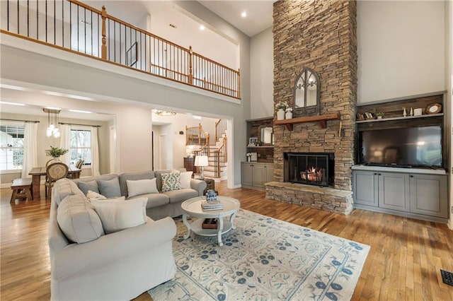 living room featuring baseboards, a towering ceiling, hardwood / wood-style floors, stairs, and a stone fireplace