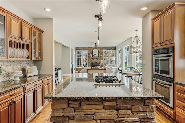 kitchen with stainless steel appliances, a fireplace, light wood-style floors, and decorative backsplash