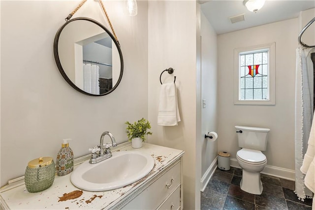 bathroom featuring toilet, stone tile floors, visible vents, baseboards, and vanity