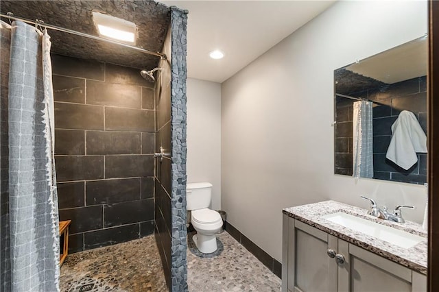 bathroom featuring toilet, recessed lighting, vanity, baseboards, and tiled shower