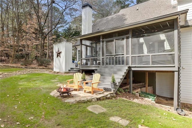 back of property with a yard, a sunroom, a shed, an outdoor structure, and a fire pit