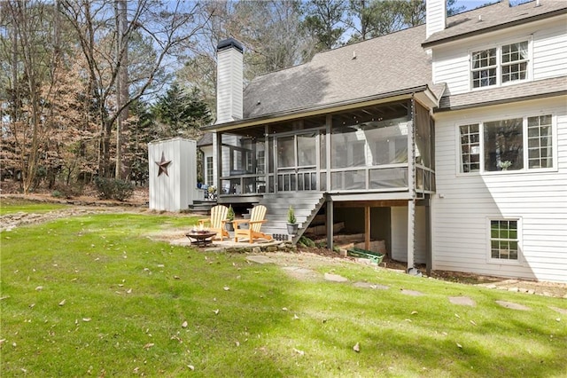 back of property featuring an outdoor fire pit, a sunroom, a chimney, a yard, and an outdoor structure