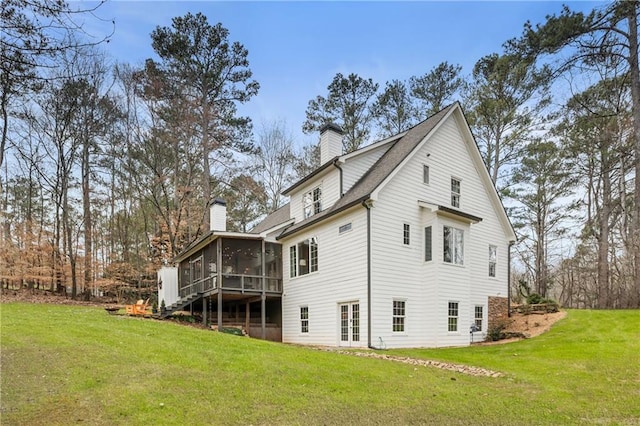 rear view of house featuring a lawn, a chimney, and a sunroom