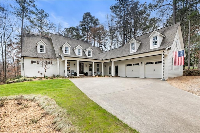 cape cod home featuring a shingled roof, covered porch, a garage, driveway, and a front lawn