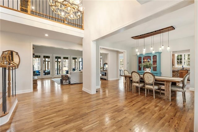 dining space with baseboards, a high ceiling, french doors, light wood-style floors, and a chandelier