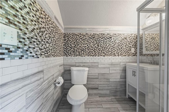 bathroom featuring vanity, a textured wall, toilet, and tile walls