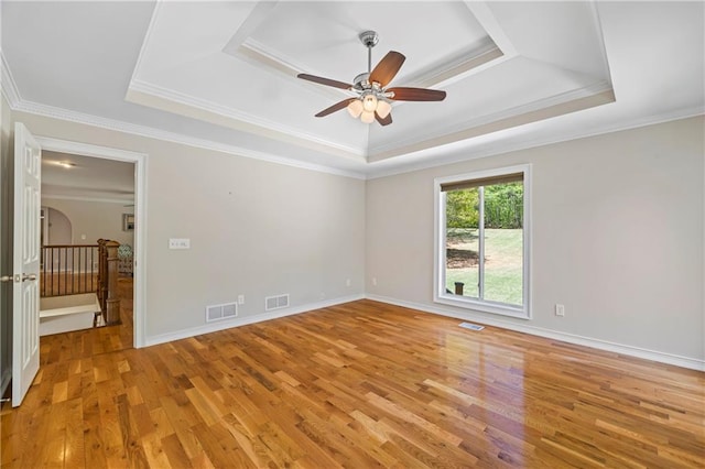 spare room with visible vents, a ceiling fan, light wood finished floors, and a tray ceiling