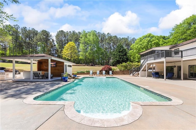 outdoor pool with a wooden deck, stairs, an outdoor structure, and a patio area