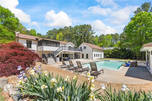 outdoor pool with a sunroom, a patio area, stairway, and a deck