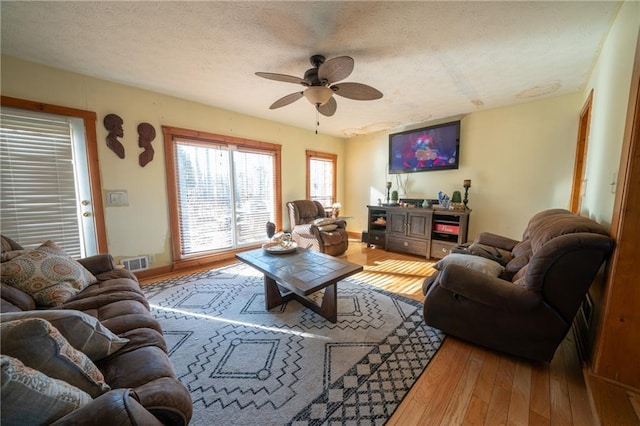 living room featuring hardwood / wood-style flooring, ceiling fan, and a textured ceiling