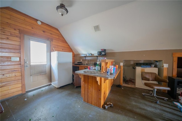 kitchen featuring a breakfast bar, wood walls, sink, white fridge, and kitchen peninsula