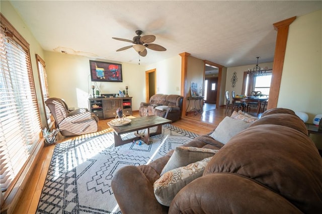 living room with ceiling fan with notable chandelier and light hardwood / wood-style flooring