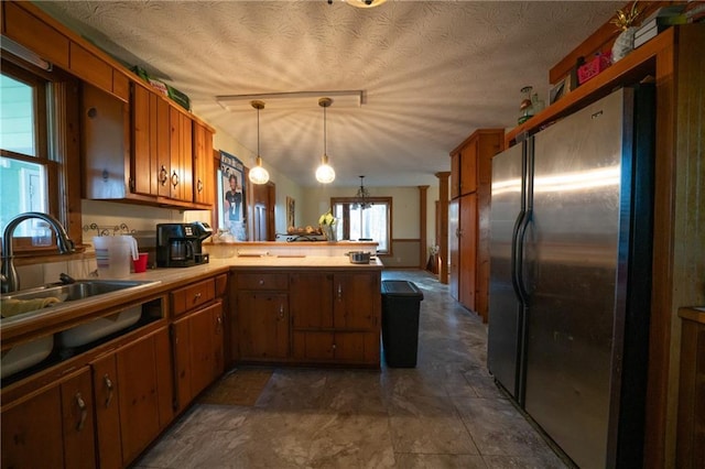 kitchen featuring pendant lighting, sink, a textured ceiling, kitchen peninsula, and stainless steel refrigerator