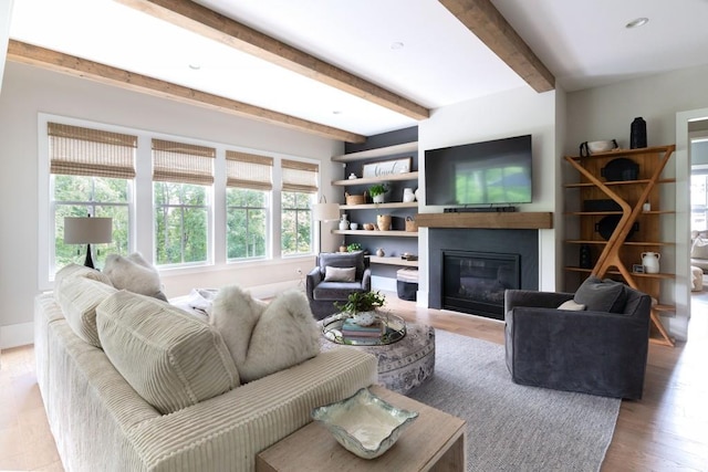 living room featuring a glass covered fireplace, wood finished floors, and beamed ceiling