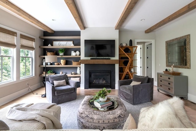 living room with a glass covered fireplace, baseboards, beam ceiling, and wood finished floors