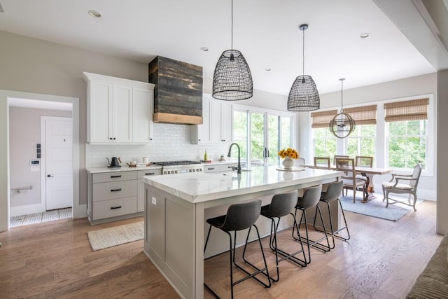 kitchen with decorative backsplash, light wood-style floors, an island with sink, light countertops, and a sink