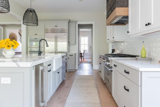 kitchen featuring decorative backsplash, decorative light fixtures, light stone counters, premium appliances, and custom range hood