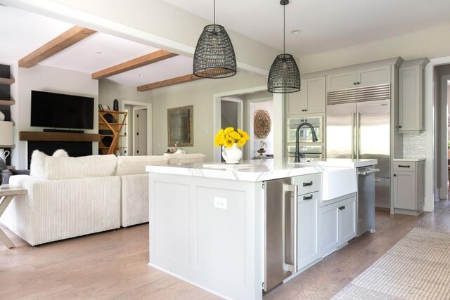 kitchen featuring pendant lighting, light stone counters, open floor plan, stainless steel appliances, and an island with sink