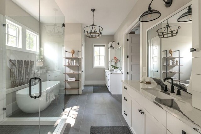 bathroom featuring a freestanding bath, two vanities, a sink, baseboards, and a notable chandelier