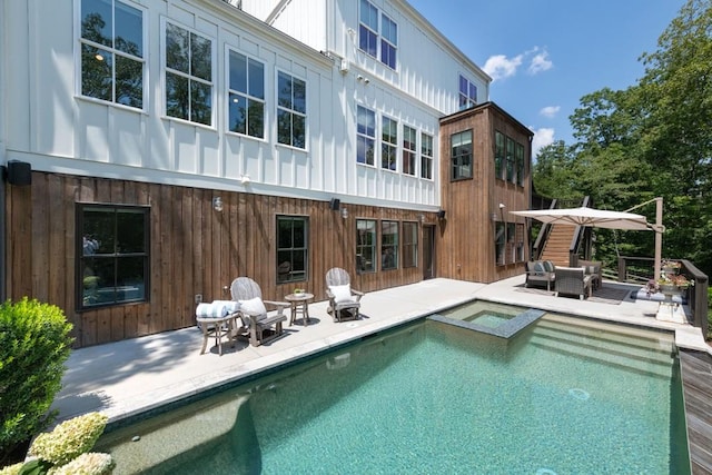 back of property with board and batten siding, an in ground hot tub, a patio area, and an outdoor pool