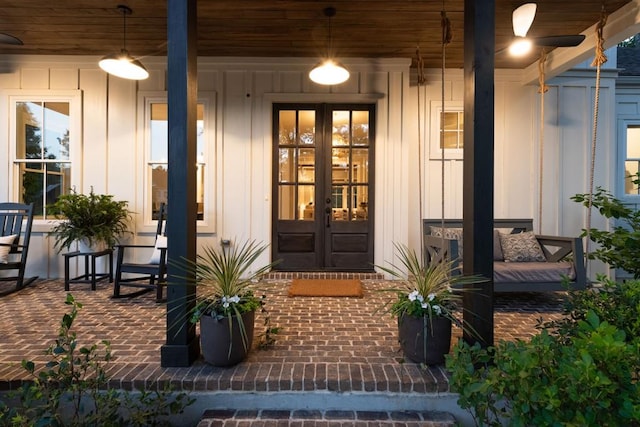 view of exterior entry with board and batten siding, french doors, and covered porch