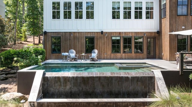 rear view of property featuring an in ground hot tub, a patio area, and an outdoor pool