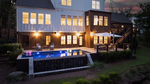 back of property featuring fence, a shingled roof, board and batten siding, a patio area, and stairway