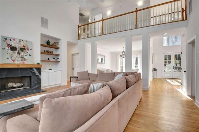 living room featuring built in shelves, french doors, light hardwood / wood-style flooring, a high end fireplace, and a high ceiling