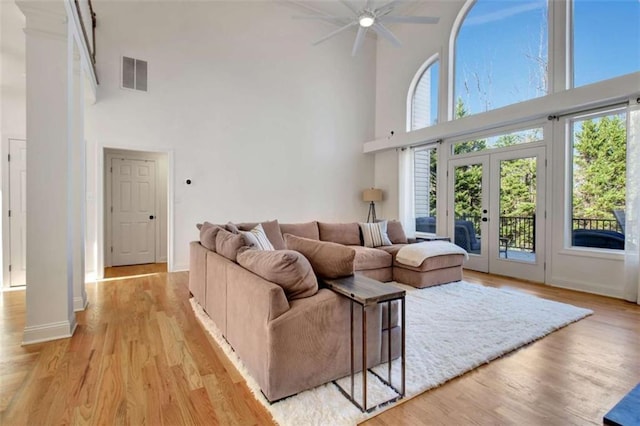 living room with a towering ceiling, light wood-type flooring, and french doors