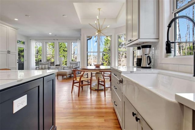 kitchen with pendant lighting, sink, white cabinetry, a notable chandelier, and light hardwood / wood-style floors