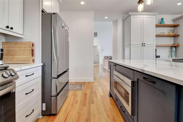 kitchen featuring appliances with stainless steel finishes, white cabinets, decorative backsplash, light stone counters, and light hardwood / wood-style floors