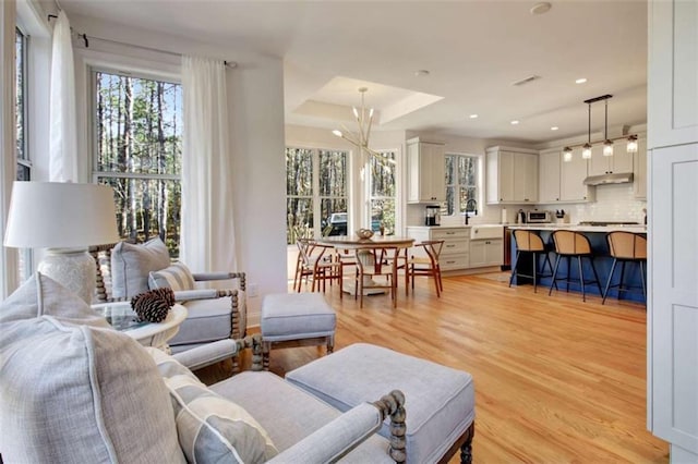 living room featuring a notable chandelier, sink, light hardwood / wood-style floors, and a raised ceiling