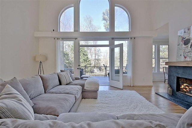 living room with french doors, light wood-type flooring, a fireplace, and a towering ceiling