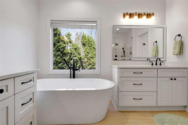 bathroom with a bathing tub, plenty of natural light, wood-type flooring, and vanity