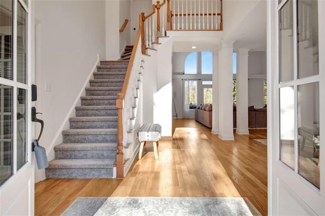 entryway featuring a towering ceiling, light hardwood / wood-style floors, and ornate columns