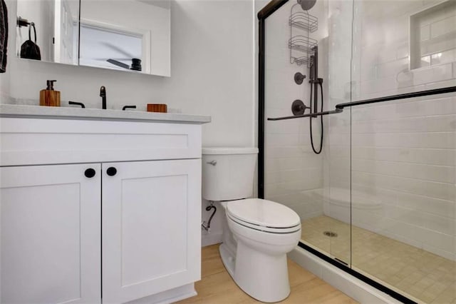 bathroom with wood-type flooring, a shower with shower door, vanity, and toilet